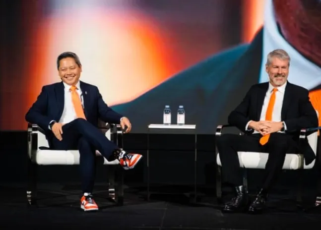 Phong Le and Michael Saylor seated on stage at a MicroStrategy event, both wearing orange ties