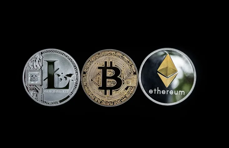 Silver Litecoin, gold Bitcoin, and Ethereum coins lined up on black background, representing major cryptocurrencies