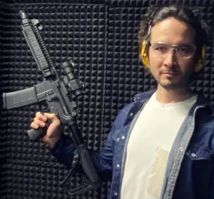 Man holding a firearm at an indoor shooting range, referenced in reports related to the Meta Whale pyramid scheme controversy.