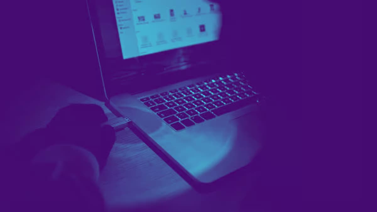 Person inserting USB flash drive into laptop with cyber-themed blue and purple overlay representing cybersecurity and data transfer