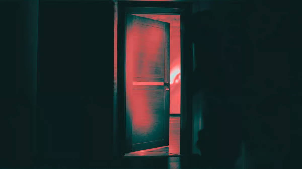A slightly open wooden door in a dark room with an eerie red light glowing from the inside.