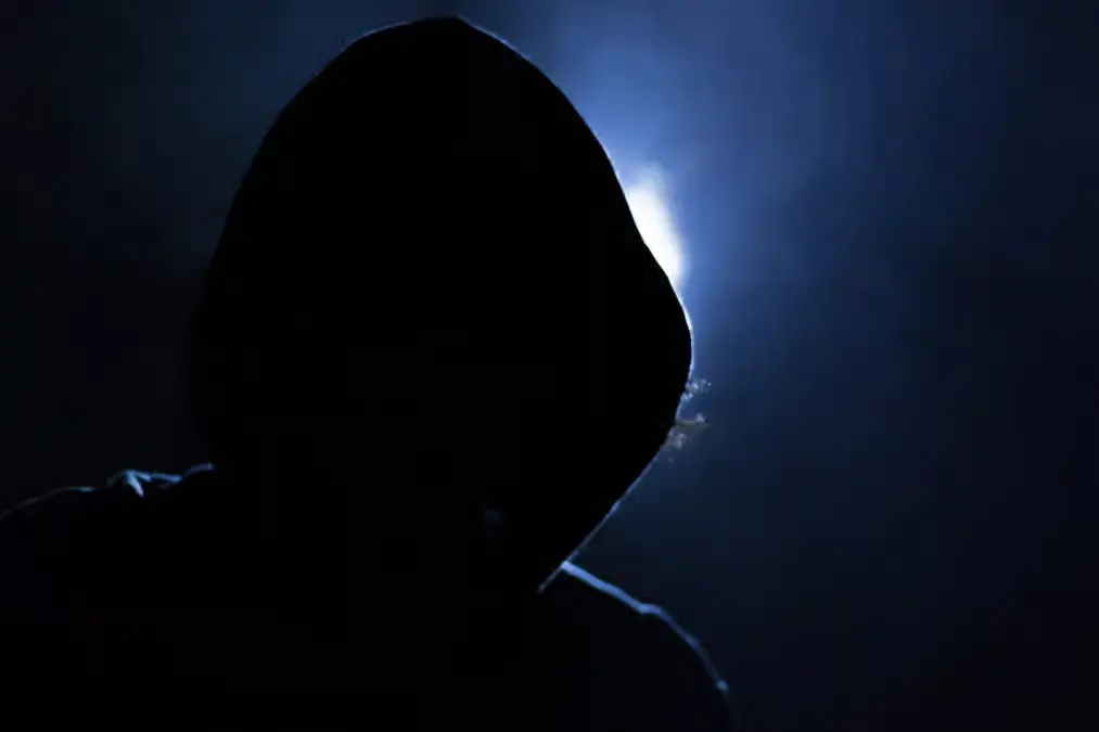 Anonymous hooded hacker silhouette in a dark environment representing cybercrime, online fraud, hacking threats, and digital security risks.