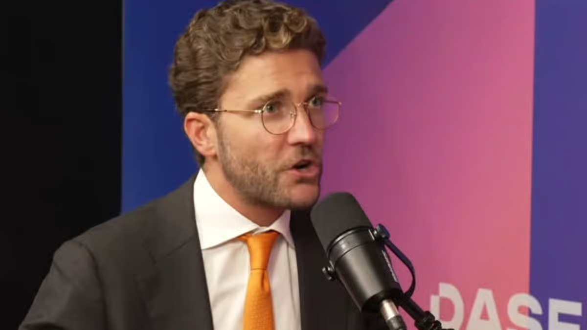 Business executive in a suit and orange tie speaking into a microphone during a podcast interview session.