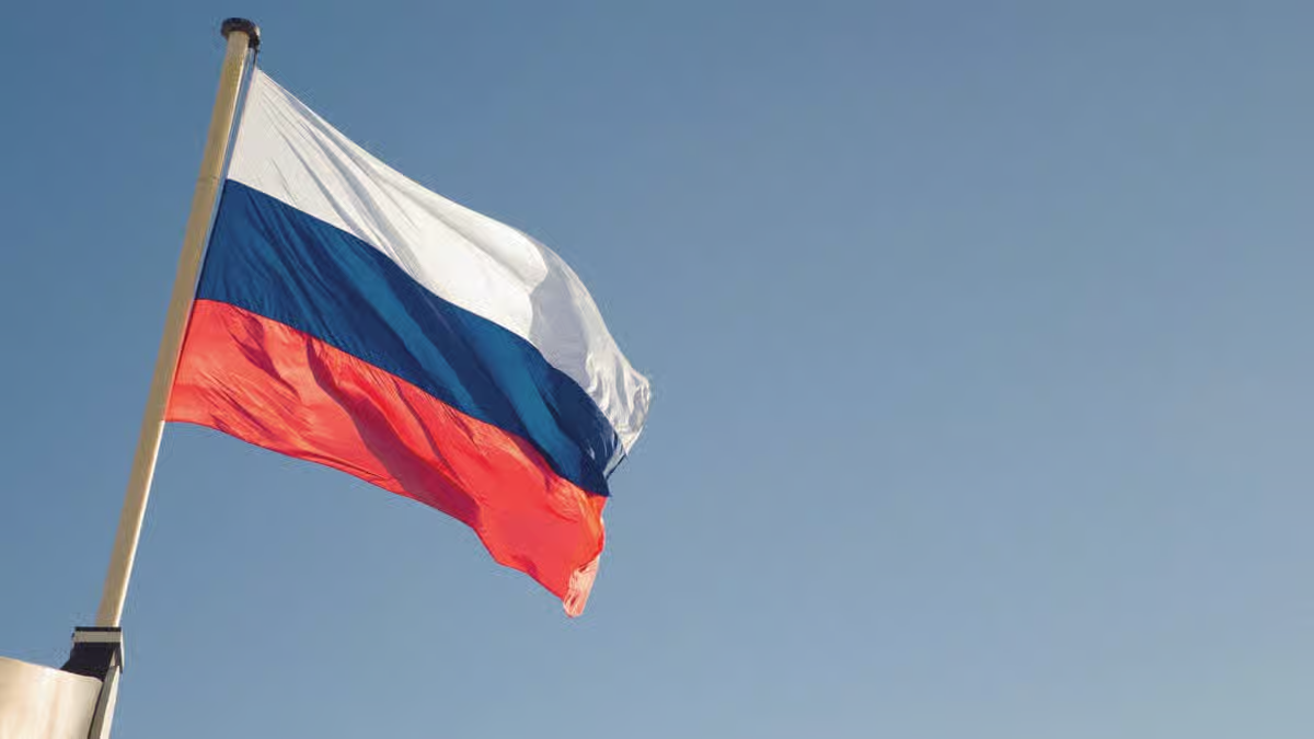 The white, blue, and red tricolor national flag of Russia waving on a flagpole against a clear blue sky.