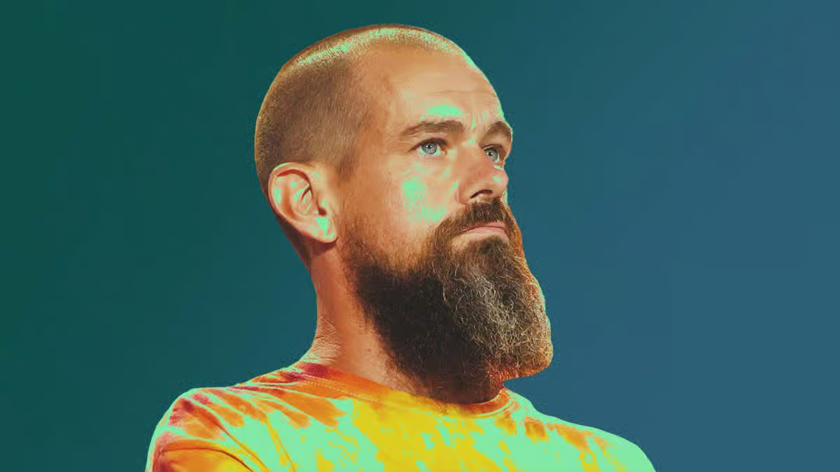 Portrait of Jack Dorsey with a long beard, wearing a bright orange and green tie-dye shirt against a teal gradient background.