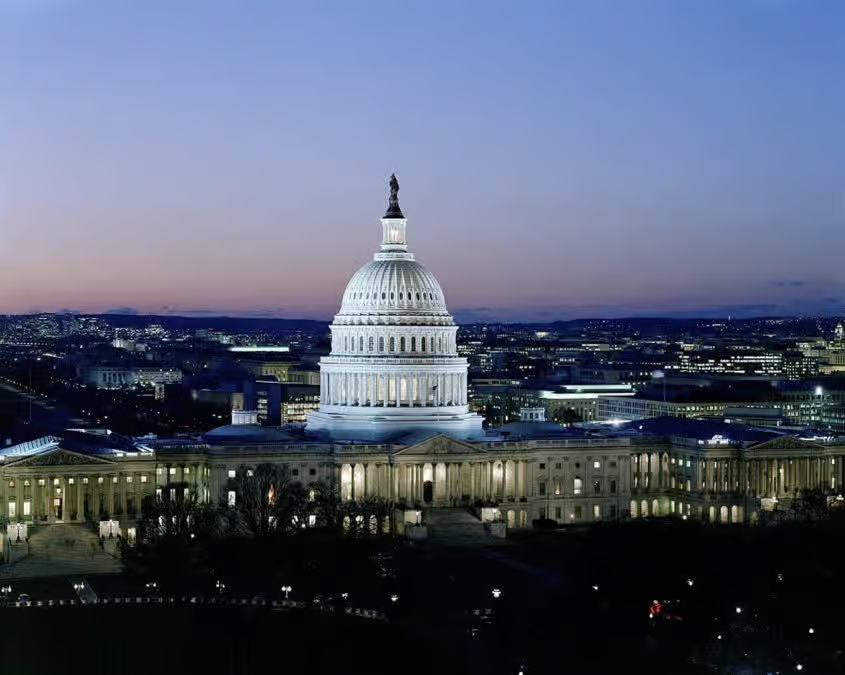 The illuminated United States Capitol building in Washington D.C. during twilight, with city lights visible in the background.
