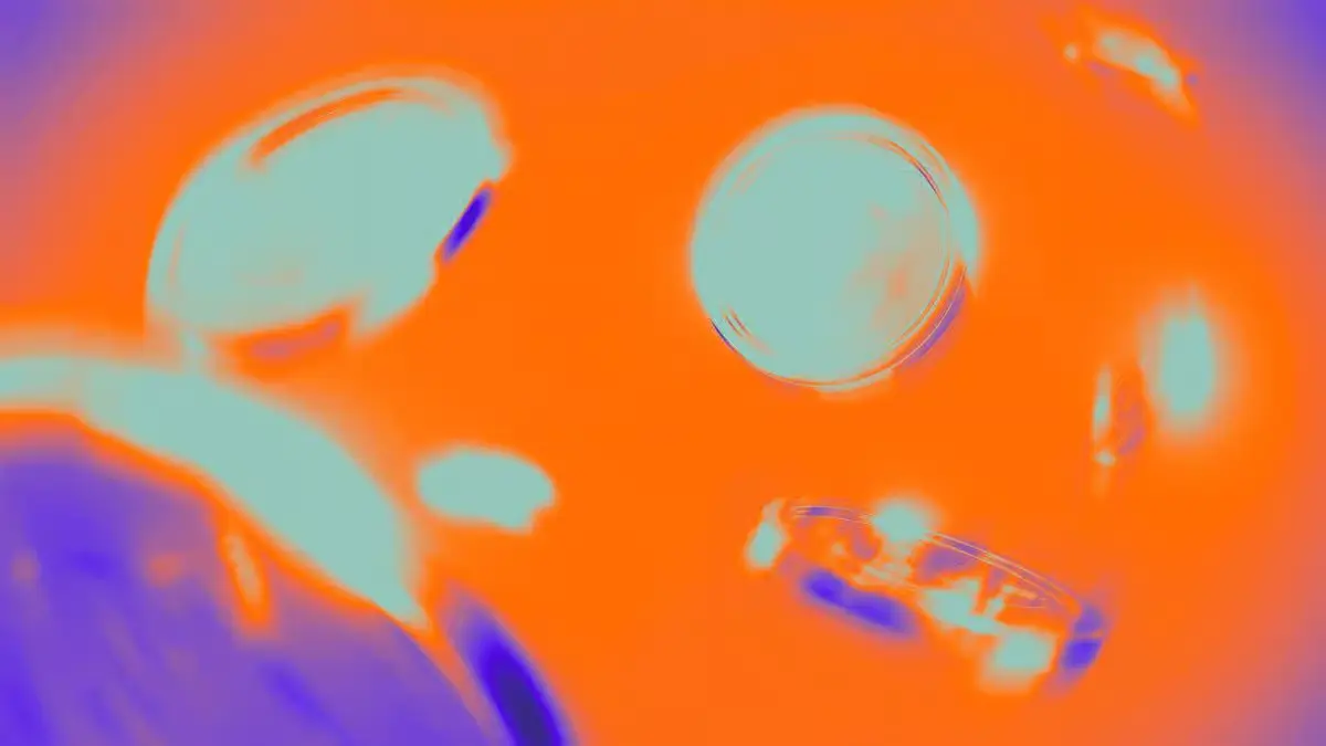 Abstract vibrant thermal heat-map style graphic showing floating metallic coins on a bright orange background.
