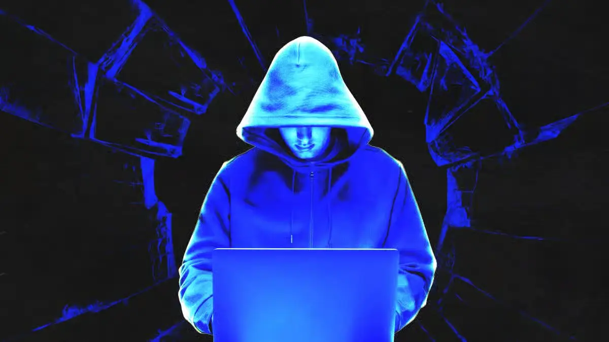 Anonymous hooded hacker sitting behind laptop glowing with blue neon light