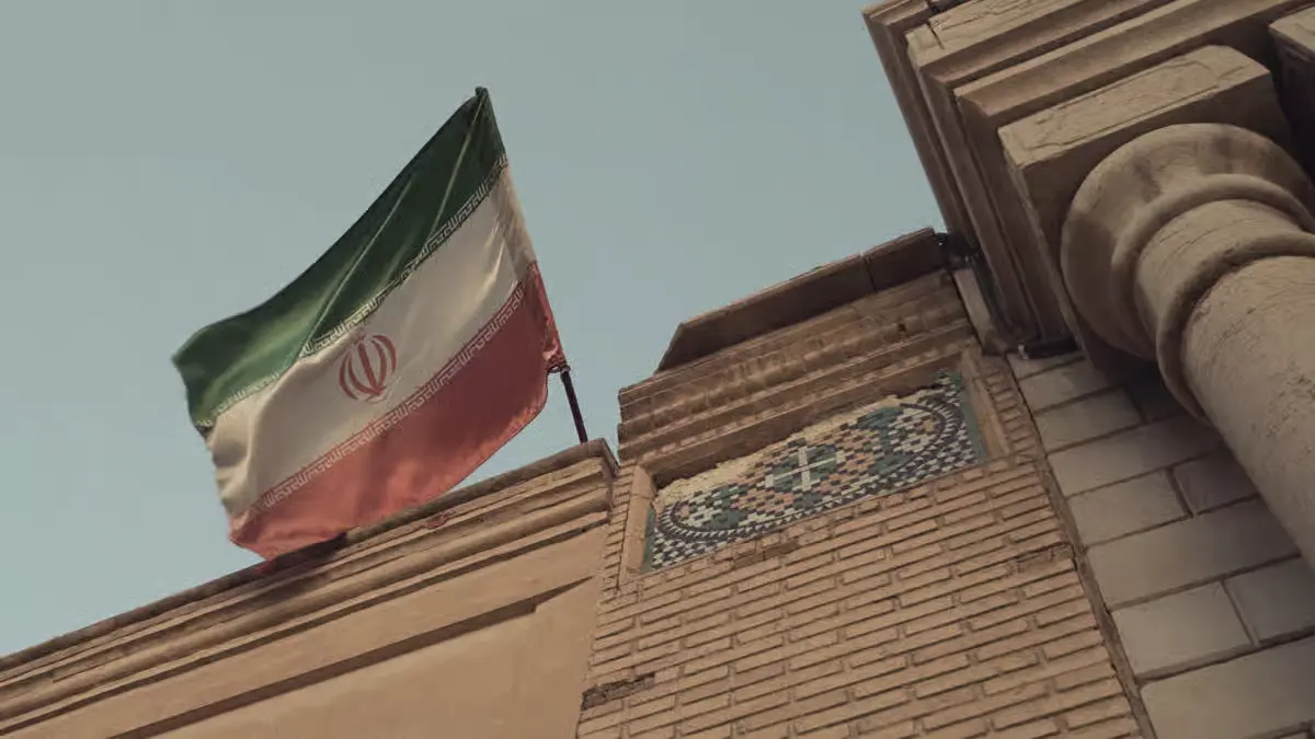Iranian flag flying beside an ornate historic building under a clear sky.