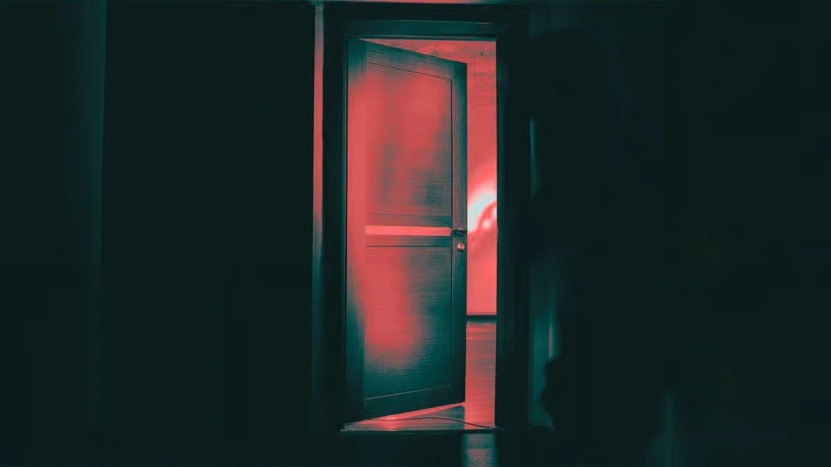 An open wooden door emitting a bright red glow into a dark room, creating a mysterious atmosphere.