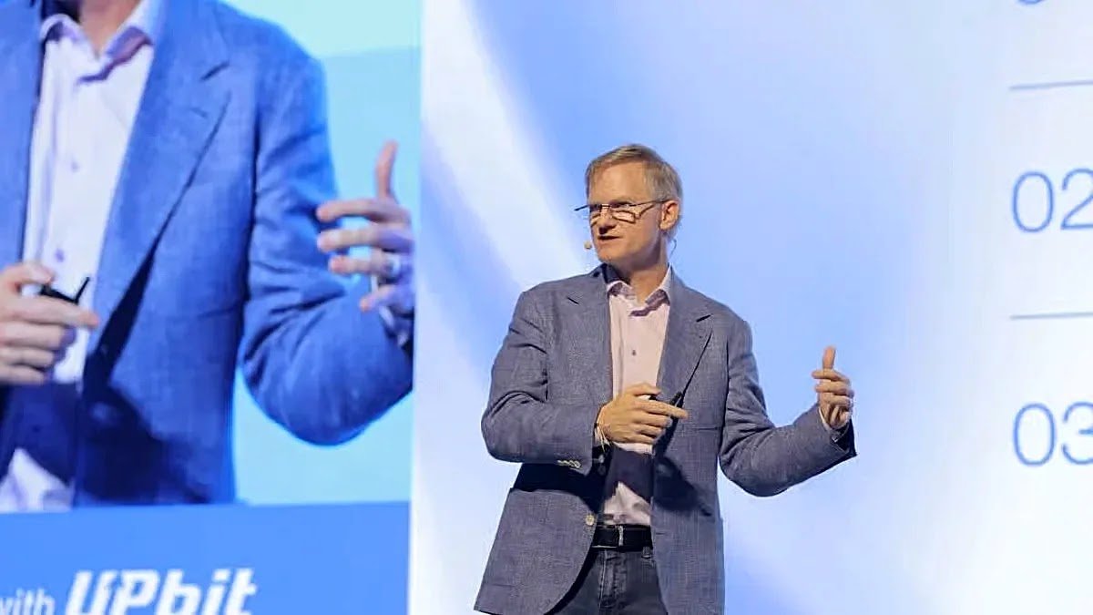 Speaker wearing glasses and a blue blazer giving a keynote presentation on stage at an Upbit tech conference.